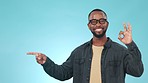 Pointing, option and face of black man in a studio with choice, decision or comparison expression. Happy, smile and portrait of young African male model with an ok gesture isolated by blue background