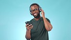 Headphones, phone and young black man in a studio listening to music, album or playlist. Happy, dancing and African male model streaming a song or radio on cellphone isolated by blue background.