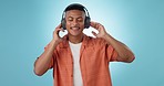 Headphones, dancing and young man in a studio listening to music, playlist or album for entertainment. Happy, smile and male model from Mexico streaming or radio with technology by blue background.