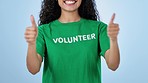 Hands, thumbs up and volunteer tshirt of woman in studio isolated on blue background. Closeup, like sign and happy person volunteering, success and support charity, nonprofit NGO or community service