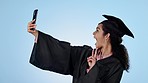 Selfie, celebration and woman with graduation, post and wink with education on a blue studio background. Person, model and student with cellphone, social media and post with peace sign and excited