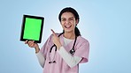 Doctor, tablet and point in happiness to greenscreen for promotion of healthcare mock up in studio. Female nurse, medical professional and excited for announcement by social media on blue background