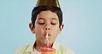 Blowing candle, child and a cupcake for a birthday, celebration or a wish on a studio background. Happy, face portrait and a hungry boy kid with party food, cake or dessert for a present or event