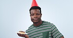 Man, frustrated and lonely for birthday with dessert, candle blow and blue studio background. African person, shakes head and unhappy for alone with confetti, party hat and casual style in portrait 