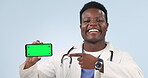 Doctor, phone and black man pointing to green screen in studio isolated on a blue background mockup space. Smartphone, tracking markers and hand of happy medical professional advertising healthcare