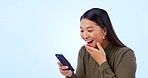 Asian woman, cellphone and excited with happiness, laughing and on blue studio background. Social media, streaming or communication with memes, funny and comic for conversation, mobile games and chat