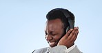 Happy black man, face and headphones listening to music against a blue studio background. Excited African businessman smile and enjoying audio streaming, sound or dancing to podcast on mockup space