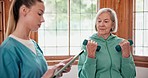 Senior woman with weights for exercise with physiotherapist at physical therapy clinic for rehabilitation. Female healthcare worker with tablet helping elderly patient with arm workout for mobility.