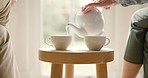 Hands, cup and pouring from a teapot closeup in a home during a visit between friends in a retirement home. Table, drink and warm beverage with elderly people in a house or apartment together