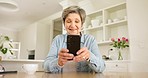 Phone, smile and senior woman in the kitchen networking on social media, mobile app or the internet. Technology, happy and elderly female person in retirement scroll on cellphone in modern home.