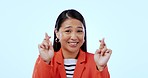 Asian woman, cross fingers and studio with hope, face or luck for results by blue background. Japanese person, hands and sign language for business deal with emoji, wish or anxiety for announcement