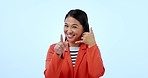 Face, smile and call me with an asian woman pointing at you in studio on a blue background for communication. Portrait, hand phone and gesture with a happy young person networking on her mobile