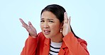 Face, confused and hearing with an asian woman in studio on a blue background listening to gossip. Portrait, frustrated or annoyed with a young person cupping her ear for communication or sound