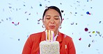 Woman, cake and blow candles in studio, confetti and birthday celebration with smile by blue background. Asian girl, party or event with dessert, flame and happy for wish, hope or excited for glitter