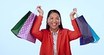 Asian woman, shopping bag and celebration in studio with smile on face for deal by blue background. Japanese girl, discount and sale with dancing, excited or saving on gift, fashion or retail product