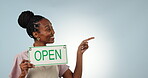 Smile, pointing and open sign with a happy black woman in studio on a gray background for advertising. Portrait, space and coffee shop with a happy young employee showing mockup for marketing
