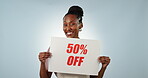 Face of business owner, sale poster or waitress in studio on blue background for 50 percent off promo. Advertising, barista or happy black woman pointing to sign on paper for cafe discount marketing 