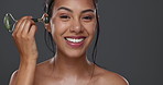 Woman, smile and facial roller for skincare or massage in studio by gray background. Happy model, cosmetics and dermatology for wellness, glow and tool for treatment on skin, beauty and health