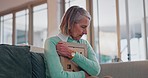 Sad senior woman, hug photo and thinking with grief, lost love and broken heart on living room sofa in home. Elderly lady, picture frame and depression for death, mourning and memory on lounge couch