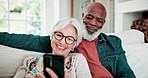 Old couple on sofa with phone, smile and relax with love, interracial marriage and bonding in home. Social media meme, mobile app and smartphone, happy senior man and woman on couch in living room.