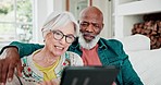 Old couple on sofa with tablet, conversation and relax with love, interracial marriage or bonding in home. Social media meme, digital app and smile, senior man and happy woman on couch in living room