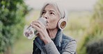 Senior woman, drinking water and fitness, outdoor exercise or running break for health, energy or wellness in nature. Elderly person with headphones, listening to music and thirsty in forest training