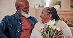 Flowers, love and senior couple in the living room talking, bonding and relaxing together at home. Smile, conversation and elderly African man and woman in retirement in the lounge of modern house.