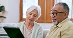 Senior couple, tablet and talking in home while reading news app, social media and ebook on sofa. Old man, woman and interracial partner scroll on digital blog, online shopping or relax in retirement