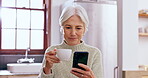 Senior, woman and phone with coffee in kitchen for social media, internet scroll or technology with relax. Elderly, person or smartphone with tea in home for peace, happiness and streaming on website