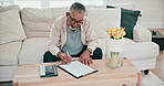 Finance, documents for insurance and a senior man planning on a sofa in the living room of his apartment. Paper, writing and home budget with an elderly person accounting for investment payment