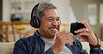 Laughing, senior man and a movie on a phone, watching a funy video or film on the internet. Happy, streaming and an elderly person with headphones, mobile and a comedy show on an app on the home sofa
