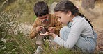 Adventure, magnifying glass and children exploring in the mountain for outdoor discovery together. Nature, fun and young kids playing with plants for research on a hike in countryside on vacation.