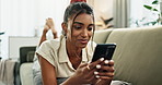 Woman, phone and lying on couch for communication with smile, conversation or typing in living room of home. Indian, person and smartphone for texting with internet or technology on sofa in lounge