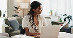 Woman, work from home and documents on computer for online research, financial planning and data report. Young worker or freelancer typing on her laptop with paperwork, bills and taxes in living room