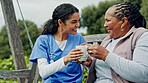 Senior woman, outdoor and nurse with coffee in nursing home garden for support and wellness. Old person, relax and happy retirement caregiver with tea, breakfast and care in the morning and park