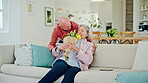 Flowers, senior couple and surprise at home with smile, love and anniversary gift with care. Happy, living room and marriage in retirement with bouquet to celebrate commitment in a home together