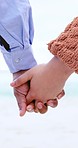 Closeup, couple holding hands and beach on walk with romance, care and love in summer sunshine. People, man and woman with support, kindness and outdoor together for holiday, ocean or adventure