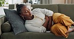 Woman, stomach and sick of pain on sofa for gut health, indigestion and gastric virus in lounge. African girl with ibs, menstruation and constipation of abdomen, endometriosis or bad bloating at home