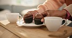 Hands, cupcake and plate on table with coffee for visit, friends or social in home. Closeup, snack and people for quality, time and together for bond in living room by delicious, chocolate or dessert