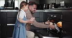 Family, baking and a father with his daughter in the kitchen to remove fresh bread from the oven. Children, love and a dad teaching his girl child hot to bake while cooking in their apartment