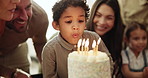 Child, candles and blow at birthday cake with family love at Jewish celebration, party together for son development. Parents, boy and kippah hat for youth dessert or sweet sugar, happy for eating