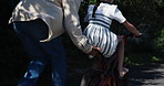 Parent, bike and child learning to ride on road, street or neighborhood in support or motivation. Closeup of father pushing kid on bicycle for bonding, teaching or riding in outdoor park together