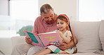 Happy, book and grandfather reading with child on a sofa in the living room of family home. Smile, love and senior man in retirement bonding, relaxing and enjoying a story with girl kid in the lounge