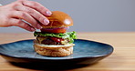 Person, hand and fast food burger on mockup space for delicious meal, snack or lunch against a gray studio background. Closeup of meat, vegetables and round bun for eating, advertising or marketing