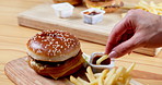 People, hands and eating fast food with chips, burger and sauce for delicious meal, snack or lunch at restaurant. Closeup of friends dipping french fries with hamburger for dinner on dining table