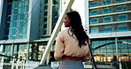 Back, wind and a business woman walking to a building in the city for the start of her work day. Thinking, commute and a young employee crossing a bridge to arrive at her urban office or workplace