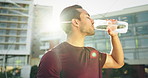 Man, drinking water and fitness in city for exercise, running break and health, energy or workout in lens flare. Young thirsty athlete, tired runner or sports person with bottle for outdoor training