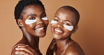 Beauty, eye pads and face of black women in studio with glowing, natural and facial routine. Smile, skincare and portrait of African female friends with cosmetic treatment by brown background.