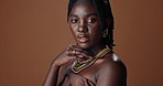Black woman, face and traditional in studio with fashion for culture, aesthetic and empowerment with hand. African person, portrait and confidence with natural beauty, necklace and brown background