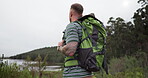 Man, backpack and travel in nature by lake or river for adventure, wellness and fitness or hiking journey. Back of hiker or person in bag trekking, explore and outdoor break for eco friendly tourism